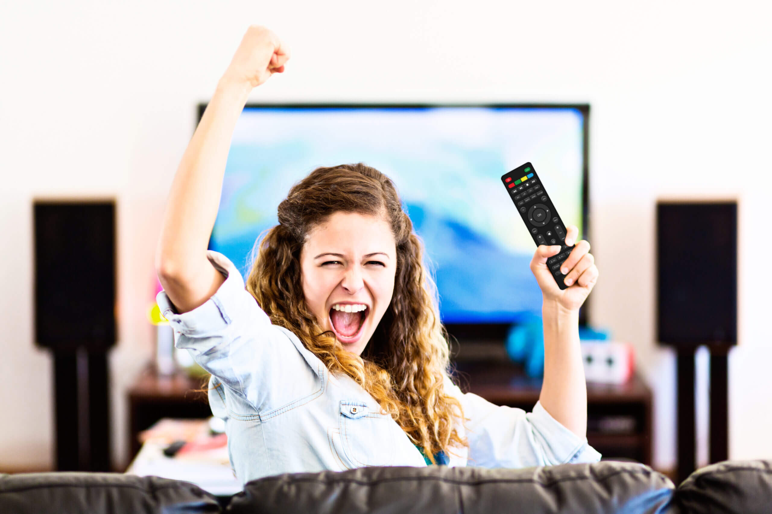 Enthusiastic young female spectator turns from TV cheering triumphantly